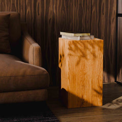 Brown leather sofa next to a wooden side table with books in a dimly lit room.