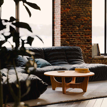 Gray sofa with a solid wood coffee table in a room with brick walls and large windows.