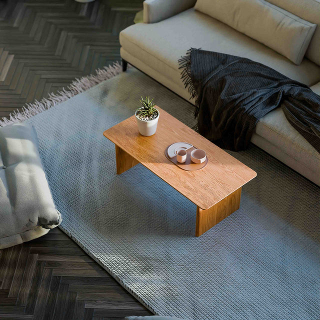 Solid oak coffee table used as a low table in a living room seating area, paired with a lounge chair and soft textiles