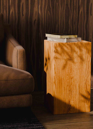 Brown leather sofa next to a wooden side table with books in a dimly lit room.