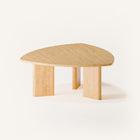 Modern solid wood coffee table in oak with clean lines and natural grain, centered in a minimalist living room with a neutral sofa and soft area rug