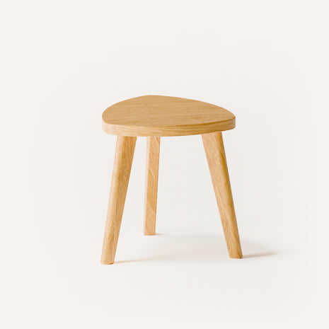 Modern solid wood stool in oak with clean lines and smooth round seat, styled in a minimalist living room with warm natural light