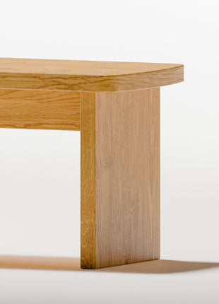 Modern solid wood nightstand in oak with clean lines and warm natural grain, styled beside a low platform bed in a minimalist bedroom setting