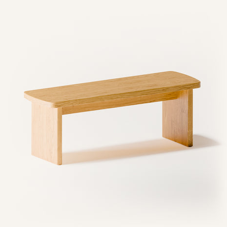 Modern solid wood nightstand in oak with clean lines and warm natural grain, styled beside a low platform bed in a minimalist bedroom setting