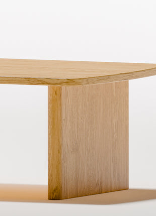 Modern solid wood coffee table in oak with clean lines and natural grain, centered in a minimalist living room with a neutral sofa and soft area rug