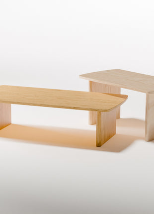 Modern solid wood coffee table in oak with clean lines and natural grain, centered in a minimalist living room with a neutral sofa and soft area rug