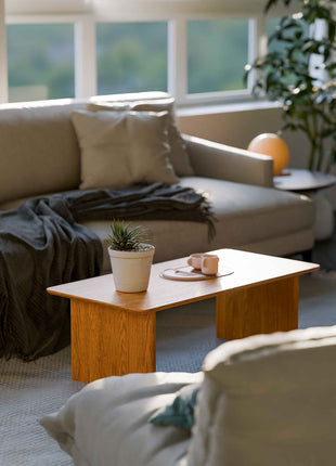 Modern solid wood coffee table in oak with clean lines and natural grain, centered in a minimalist living room with a neutral sofa and soft area rug