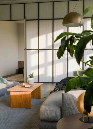Modern wood coffee table in solid oak placed in front of a light fabric sofa, styled with a tray and candle in a cozy living room