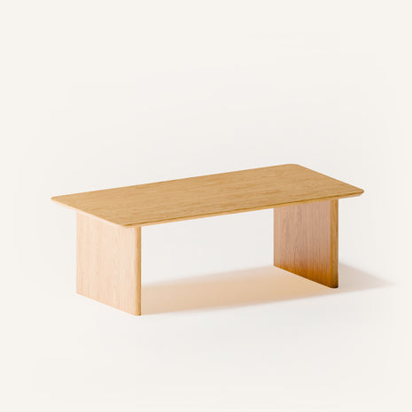 Solid oak coffee table used as a low table in a bedroom seating area, paired with a lounge chair and soft textiles