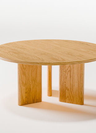 Solid oak coffee table used as a low table in a bedroom seating area, paired with a lounge chair and soft textiles