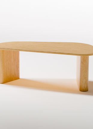 Modern solid wood coffee table in oak with clean lines and natural grain, centered in a minimalist living room with a neutral sofa and soft area rug