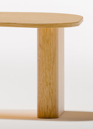 Modern solid wood coffee table in oak with clean lines and natural grain, centered in a minimalist living room with a neutral sofa and soft area rug