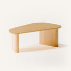 Modern solid wood coffee table in oak with clean lines and natural grain, centered in a minimalist living room with a neutral sofa and soft area rug